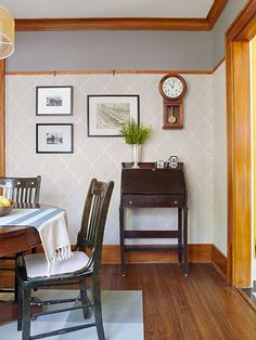 a dining room table with chairs and a clock on the wall above it in front of a window