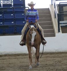 a woman riding on the back of a brown and white horse in front of blue bleachers