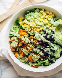 a white bowl filled with black beans, corn and guacamole dressing on top of lettuce