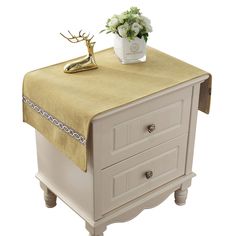 a white table with a gold cloth on it and flowers in a vase next to it