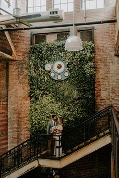 a man and woman standing on top of a stair case next to a green wall