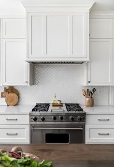 a kitchen with white cabinets, an oven and wooden cutting board on the counter top