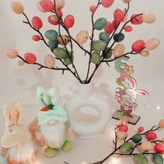 a white vase filled with lots of different colored eggs and branches in front of it