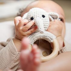 a baby is holding a crocheted elephant toy in its mouth while laying down