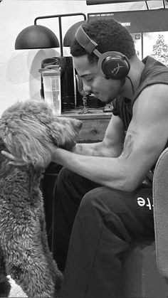 a man with headphones on sitting next to a dog and holding it's paw