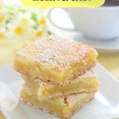 two pieces of lemon bars stacked on top of each other in front of a cup and saucer