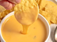 a person dipping cheese into a white bowl filled with tortilla chips and dip