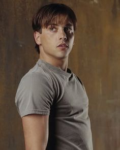 a young man poses in front of a brown wall with his hands on his hips