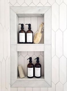 two white shelves with bottles and soaps on them in a tiled bathroom wall niche