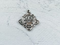 a silver colored pendant with an ornate design on the front and back side, sitting on a white surface