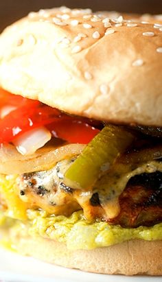 a burger with onions, peppers and other toppings on a white plate sitting on a table