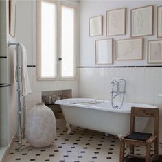 a white bath tub sitting in a bathroom next to a chair and pictures on the wall