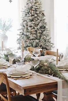 a dining room table set for christmas dinner with white plates and silverware on it