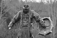 a man dressed in native american clothing holding a large object with trees in the background