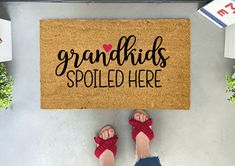 a person standing in front of a door mat that says grandkids spoiled here