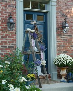 a wooden ladder with flowers on it in front of a blue door and some potted plants