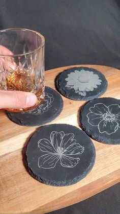 a person is holding a glass and some coasters on a wooden tray with flowers drawn on them