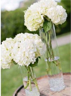 two vases filled with white flowers on top of a wooden table