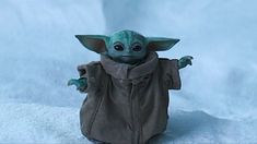 a baby yoda doll is posed on a white surface with snow in the background