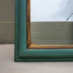 a green framed mirror sitting on top of a white counter next to a building and telephone wires