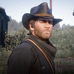 a man in a cowboy hat and scarf standing next to a wooden building on a hill