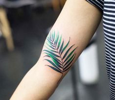 a woman's arm with a green palm leaf tattoo on the left side of her arm