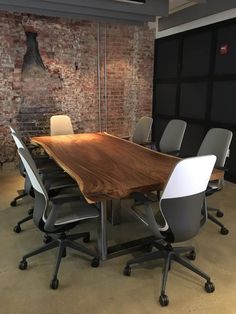 a wooden table surrounded by grey chairs in an office setting with exposed brick wall behind it