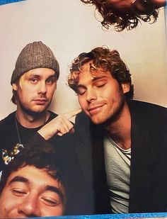 three young men are posing for the camera with their eyes closed and one is wearing a beanie