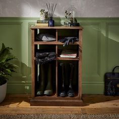 a wooden shelf filled with rain boots next to a potted plant and green wall