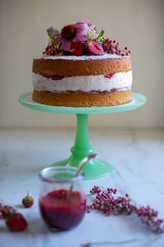 a cake sitting on top of a green cake stand next to berries and sauces