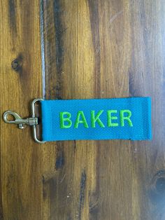 a blue keychain with the word baker on it sitting on a wooden surface