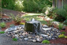 a water fountain in the middle of a graveled area with rocks and plants around it