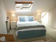 a bed sitting under a skylight in a bedroom next to a chair and lamp