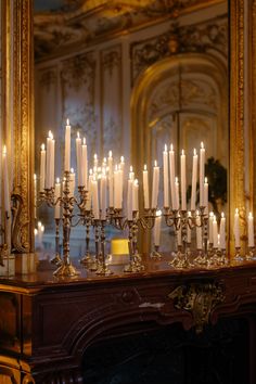 many candles are lit on a table in front of a mirror with gold trimming