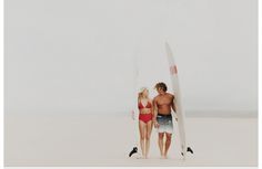 a man and woman in swimsuits holding surfboards walking on the beach together