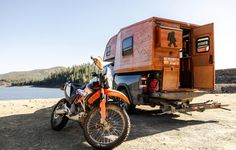 an orange dirt bike parked next to a motorcycle trailer on the side of a lake