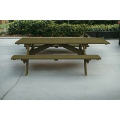 a green picnic table sitting on top of a cement floor next to bushes and shrubbery