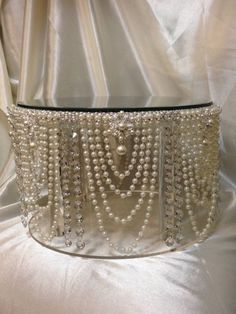 a white purse with pearls on it sitting on top of a cloth covered tablecloth