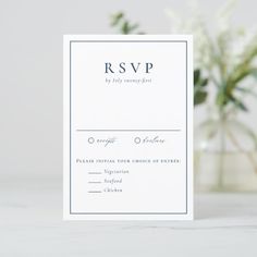 a white wedding rsvp card sitting on top of a table next to a vase with flowers