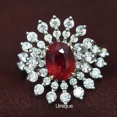 a red and white diamond ring sitting on top of a brown cloth covered surface with the words unique written below it