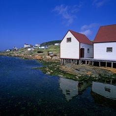 some houses are sitting on the edge of a body of water with clear blue skies in the background