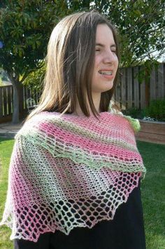 a woman wearing a pink and green crocheted shawl in front of a fence