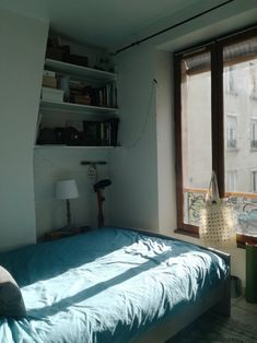 a bed sitting next to a window in a bedroom under a book shelf on top of a wall