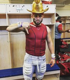 a man wearing a cowboy hat and knee pads pointing at the camera while standing in front of lockers