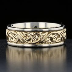 a wedding band with an intricate design on the outside and gold in the inside, against a black background