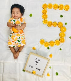 a baby laying on top of a bed next to orange slices and a sign that says time for a high - five