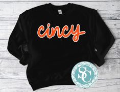 an orange and black shirt with the word cincy on it, next to a badge