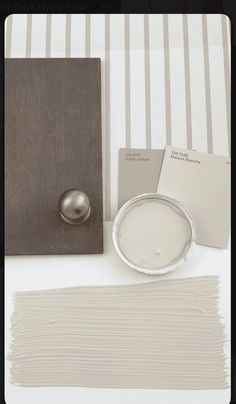 a table with some paint samples and a silver object on it's side, next to a striped wallpaper