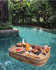 a wicker tray with food on it sitting next to a pool in the middle of a jungle