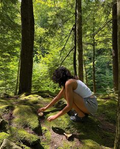 a woman kneeling down in the middle of a forest filled with green mossy rocks